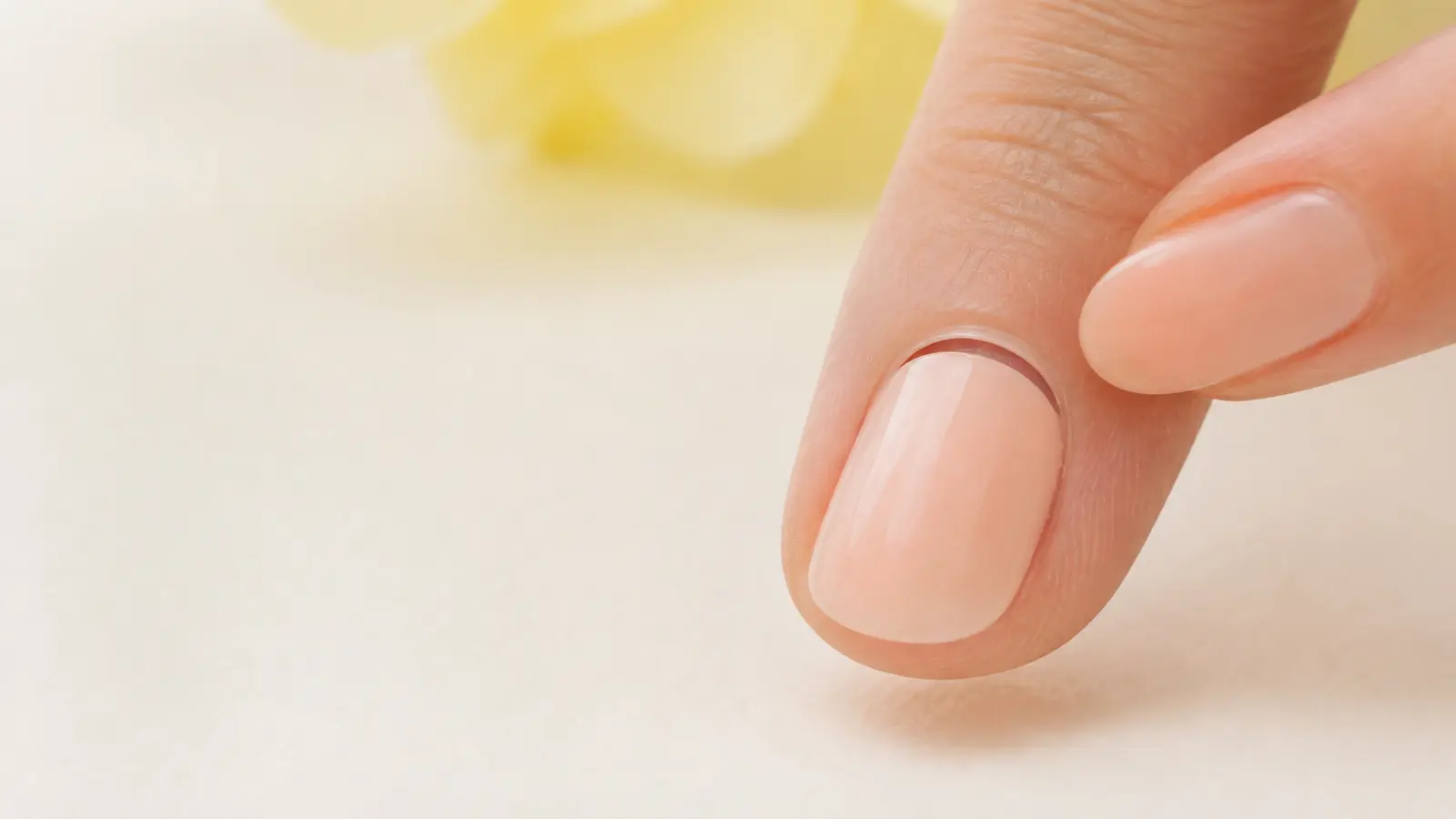 A close view of a small clean gap where a pale peach press-on has lifted at the cuticle edge.